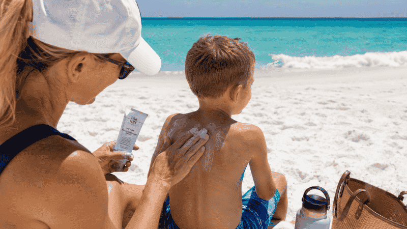 Parent applying mineral sunscreen to child on a sunny Florida beach with white sand and turquoise water