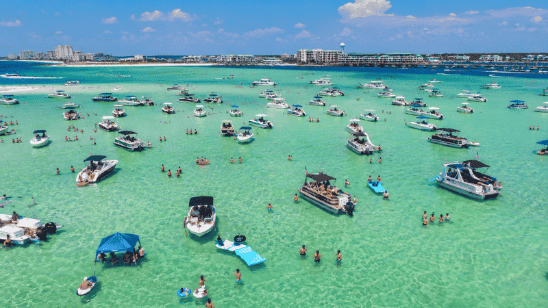Boats anchored at Crab Island sandbar in Destin Florida with people wading in shallow emerald water
