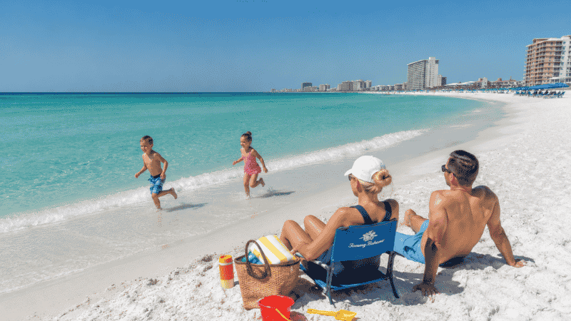 Family with young children playing on white sand beach in Destin Florida with calm emerald Gulf water