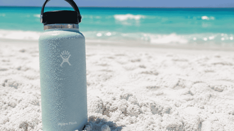 Insulated stainless steel water bottle on white sand Florida beach for hydration in summer heat
