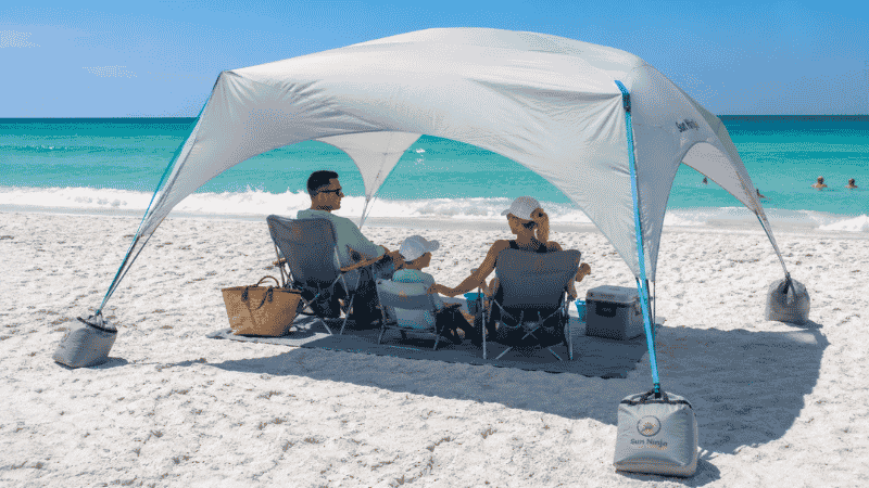 Family beach setup with pop-up shade shelter tent and sand anchors on white sand Florida beach