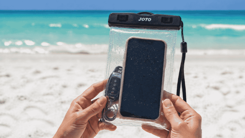 Hands holding a clear waterproof pouch with smartphone and car keys at the beach
