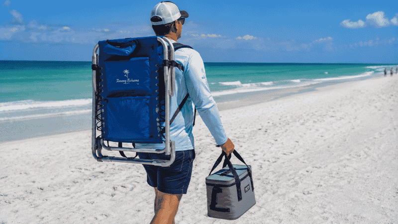 Person carrying a folded beach chair with backpack straps over both shoulders hands free on a Florida beach