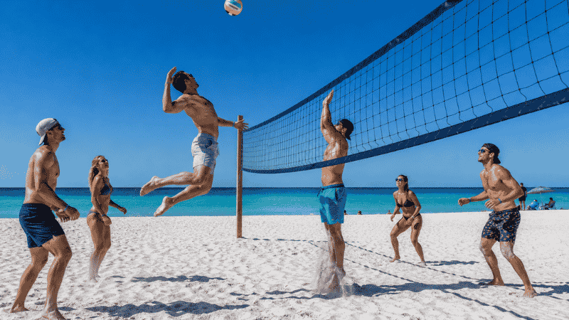 Group of adults playing beach volleyball on white sand Florida beach with turquoise Gulf water in background