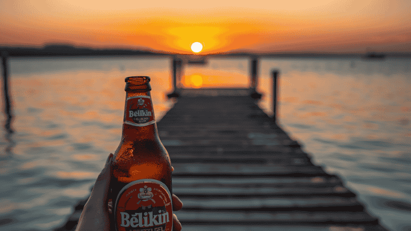 A traveler sat by the wooden pier of a resort in Belize at sunset, holding a local Belikin beer in his hand, enjoying the peaceful and safe time on the island.