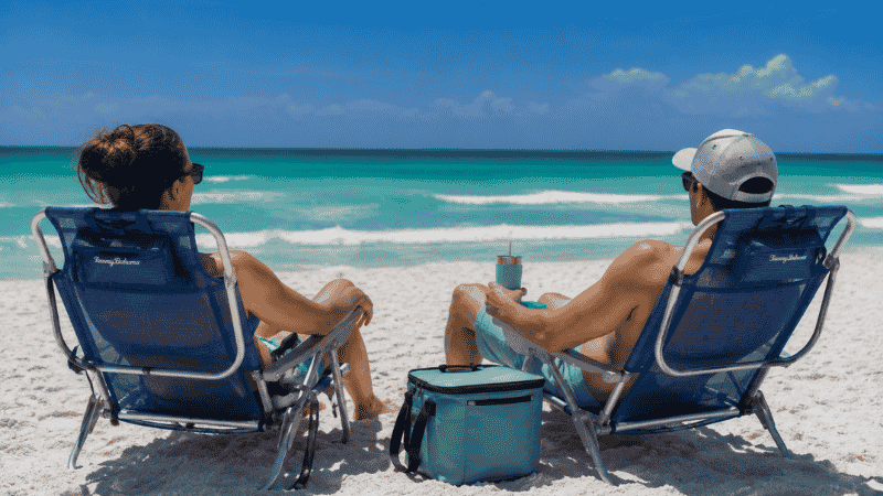 Two people relaxing in comfortable mesh beach chairs on white sand Florida Gulf Coast beach with emerald water in background