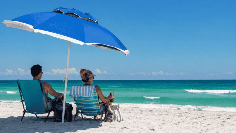 Wind-resistant beach umbrella planted in white sand on a Florida Gulf Coast beach with couple relaxing underneath