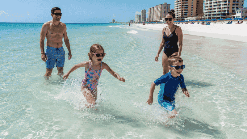 Family with children playing in shallow emerald Gulf water on white sand beach at Panama City Beach Florida