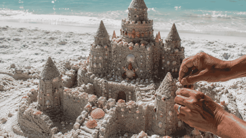 Detailed sandcastle with towers and shell decorations built with wet sand on a white beach
