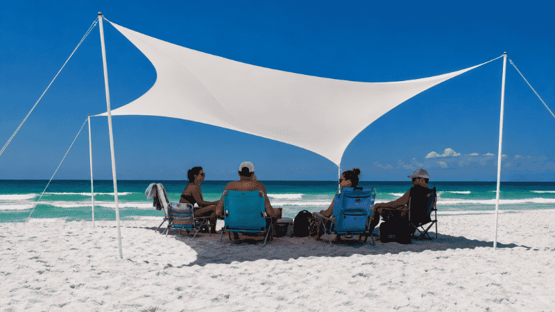 Wind-powered spandex beach shade canopy stretched between poles providing shade for a group on a Florida Panhandle beach