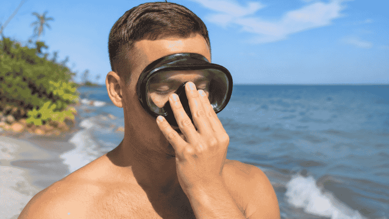 Person performing the snorkel mask suction fit test by holding mask against face without strap and inhaling through nose
