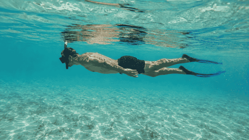 Snorkeler in correct horizontal body position floating face down in clear turquoise water with fins visible below