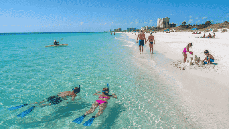 Multiple beach activities on a white sand Florida beach including snorkeling kayaking and sandcastle building