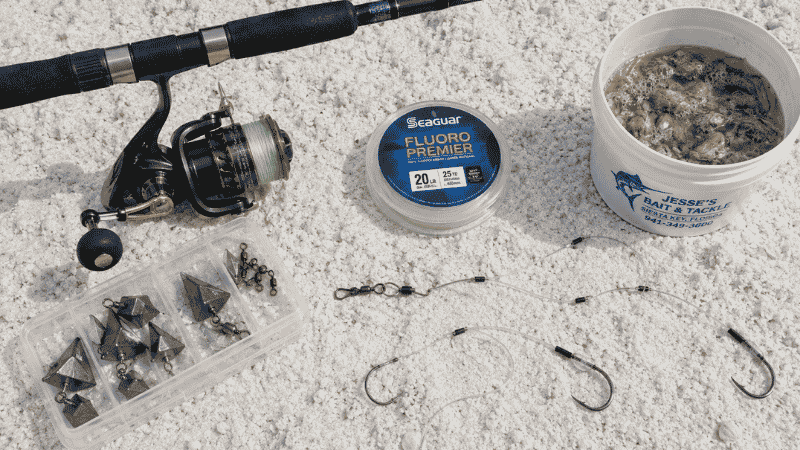 Beach fishing beginner setup flat lay showing spinning rod reel pompano rig circle hooks pyramid sinkers and bait on white sand