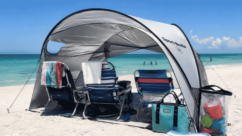 Complete family beach setup with pop-up shade tent beach chairs and cooler on white sand Florida Gulf Coast beach