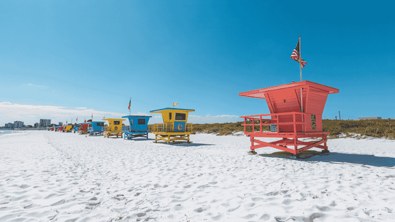 A panoramic view of Siesta Key Beach in Florida showcases the iconic pure white quartz sand beach and the colorful lifeguard watchtower.