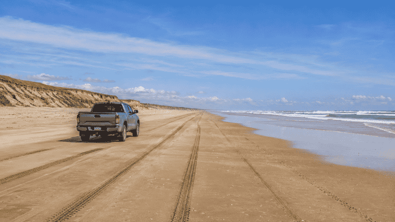 4WD truck driving on wide wild Atlantic beach at Outer Banks North Carolina with tire tracks in wet sand and remote coastline stretching to the horizon