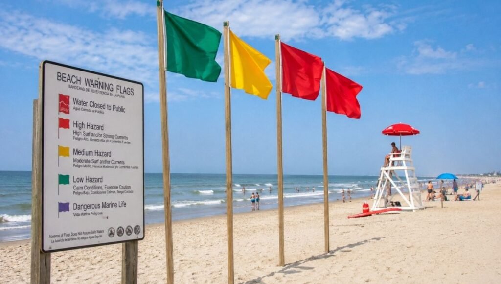 Beach warning flag system on East Coast Atlantic beach showing colored safety flags on wooden posts with lifeguard stand visible in the background