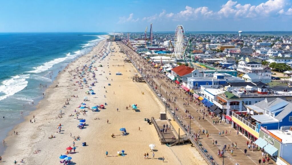 Aerial view of Jersey Shore New Jersey coastline showing wide sandy Atlantic beach with classic wooden boardwalk and colorful beach town on a bright sunny summer day